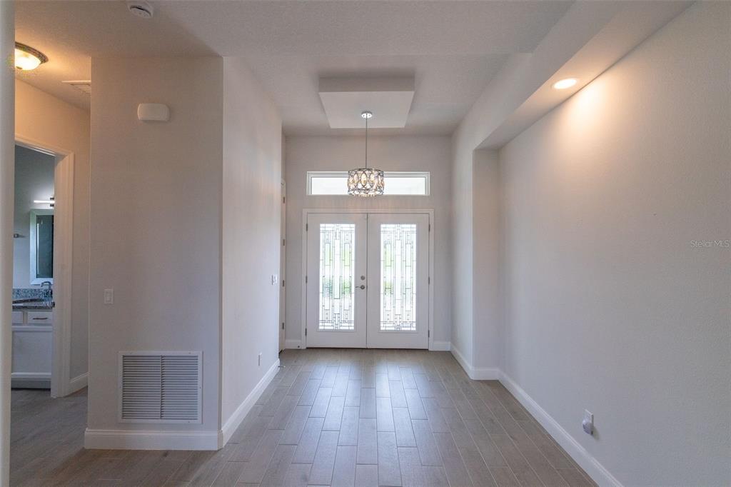 A bright entryway features double glass-paneled doors, light wood-look flooring, and a modern pendant light — 954 MEGANO BOULEVARD, DELAND, FL