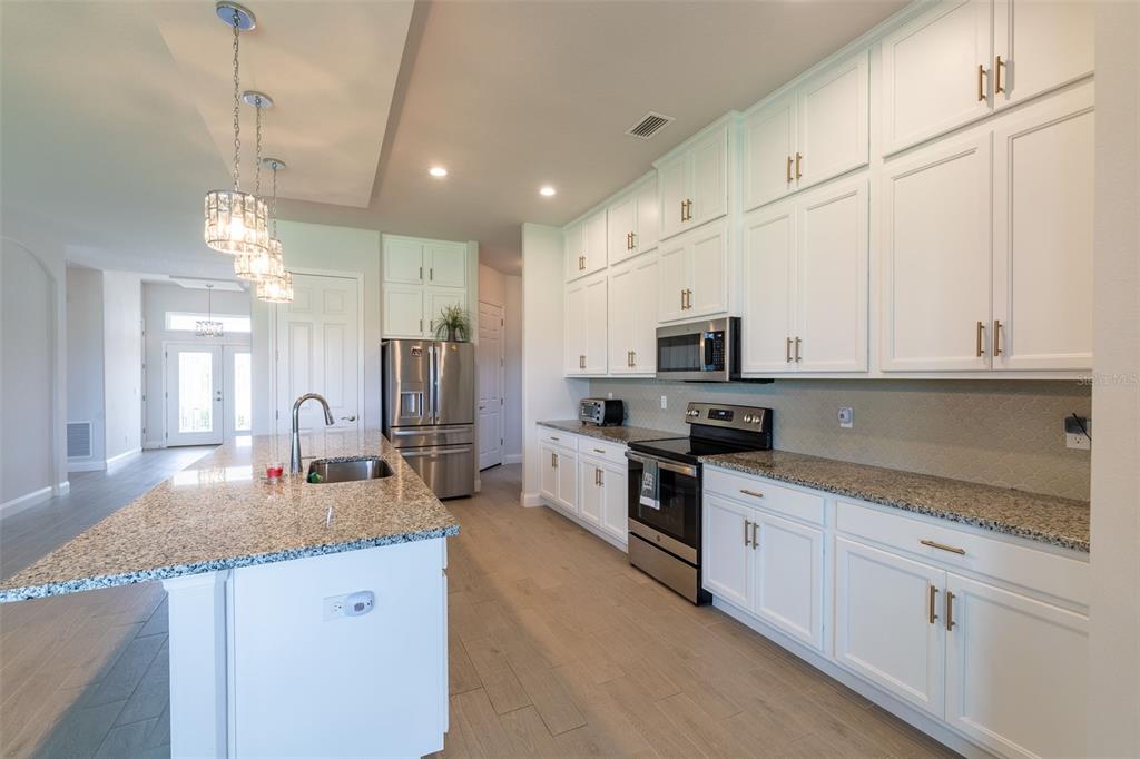 A modern kitchen features white cabinetry, granite countertops, stainless steel appliances, and a large island — 954 MEGANO BOULEVARD, DELAND, FL