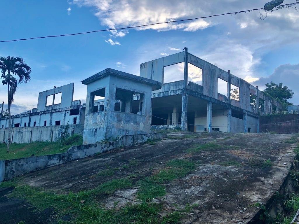 A weathered, multi-story concrete structure with open window frames sits atop a paved incline — LOT 1 PR 174 KM 22.7 SONADORA WARD, AGUAS BUENAS, PR