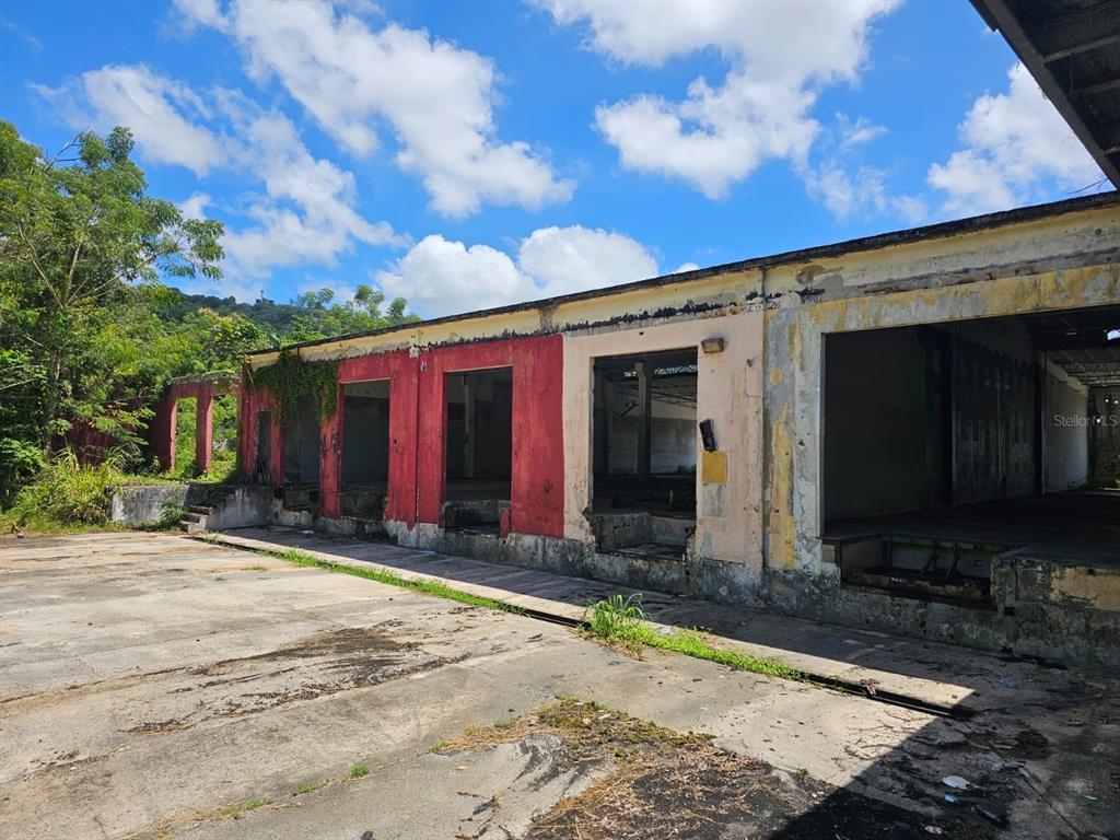 An exterior view of a dilapidated industrial building with multiple open loading bays — LOT 1 PR 174 KM 22.7 SONADORA WARD, AGUAS BUENAS, PR