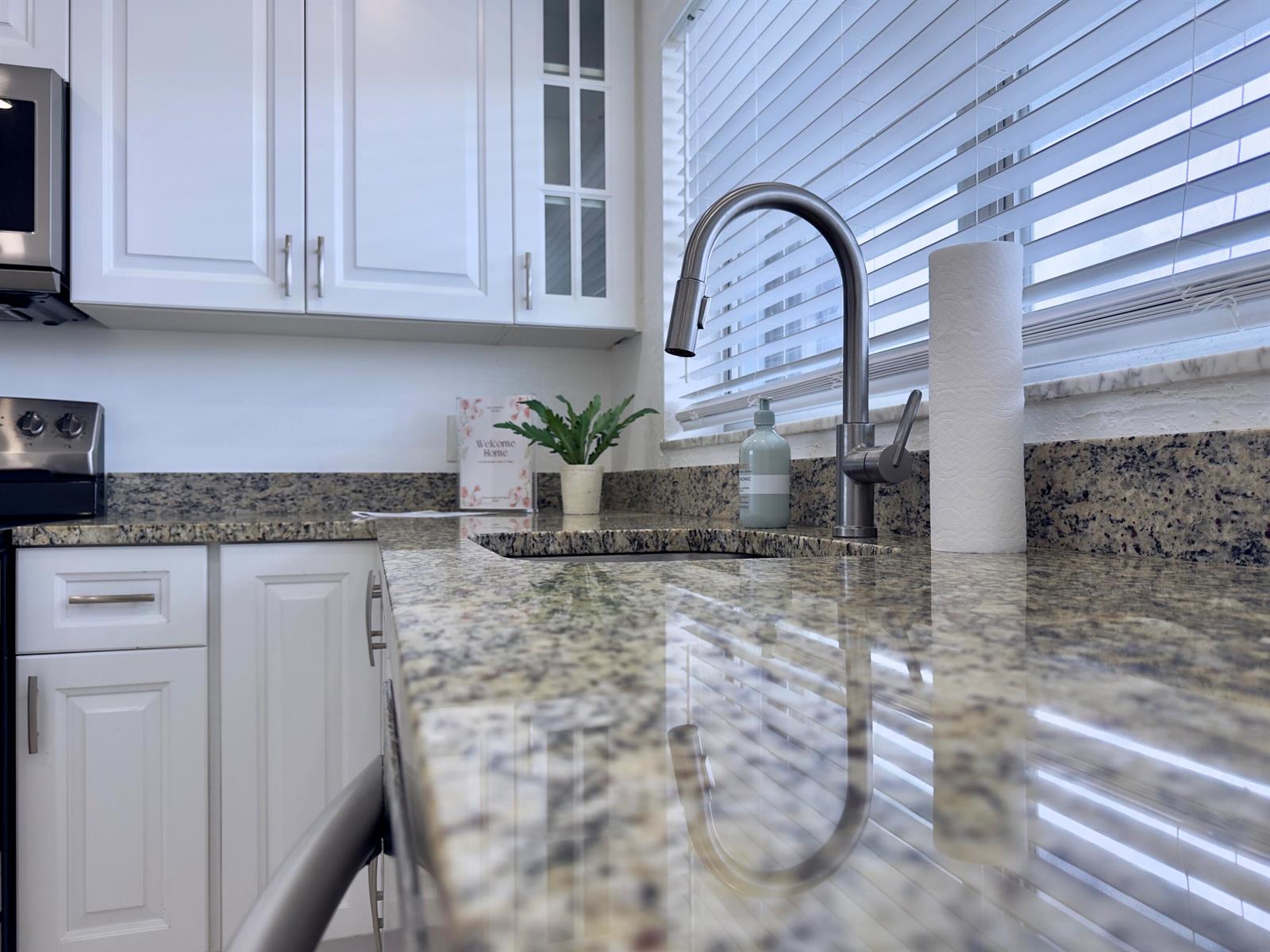 A kitchen features white cabinets, granite countertops, a stainless steel faucet, and a window — 2016 S Federal Highway # 404, Boynton Beach FL 33435, BOYNTON BEACH, FL