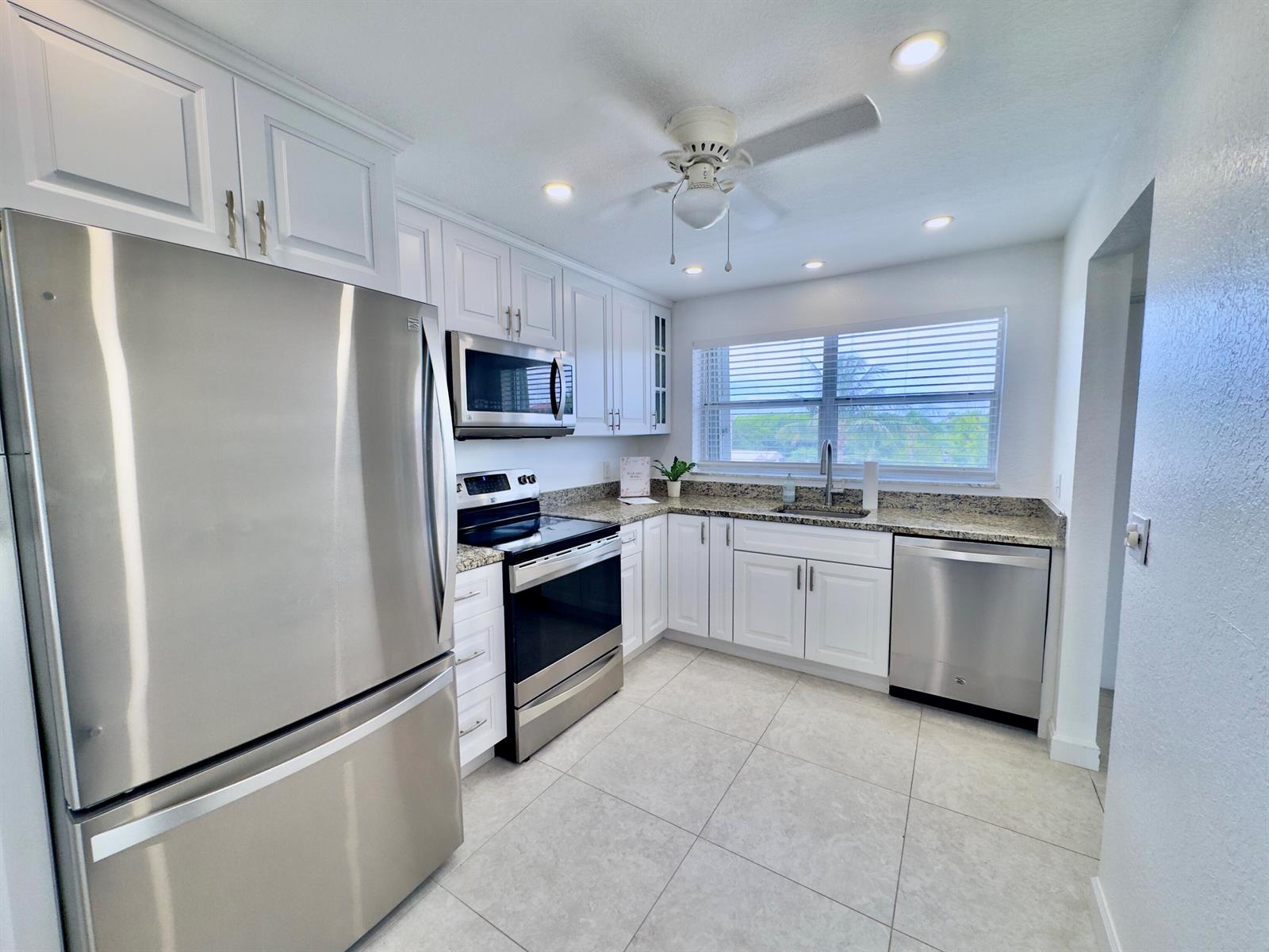 A kitchen with white cabinets, stainless steel appliances, granite countertops, and light-colored tile flooring — 2016 S Federal Highway # 404, Boynton Beach FL 33435, BOYNTON BEACH, FL