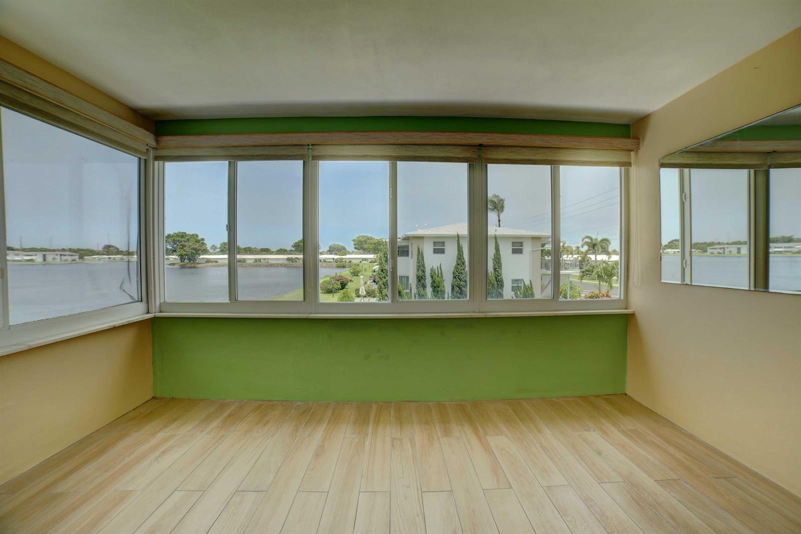 A sunroom with light wood-look tile flooring, green walls, and large windows overlooking a lake — 1118 Lake Terrace # 204, Boynton Beach FL 33426, BOYNTON BEACH, FL