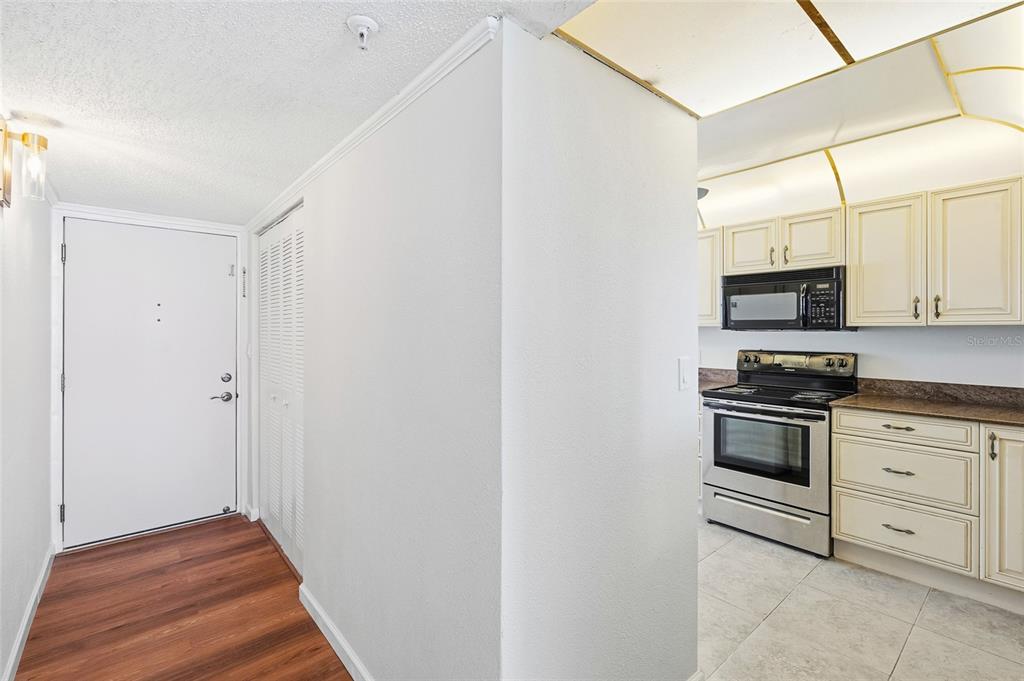 A view of an entryway with wood flooring leading into a kitchen with white cabinets — 15462 GULF BOULEVARD UNIT 601, MADEIRA BEACH, FL