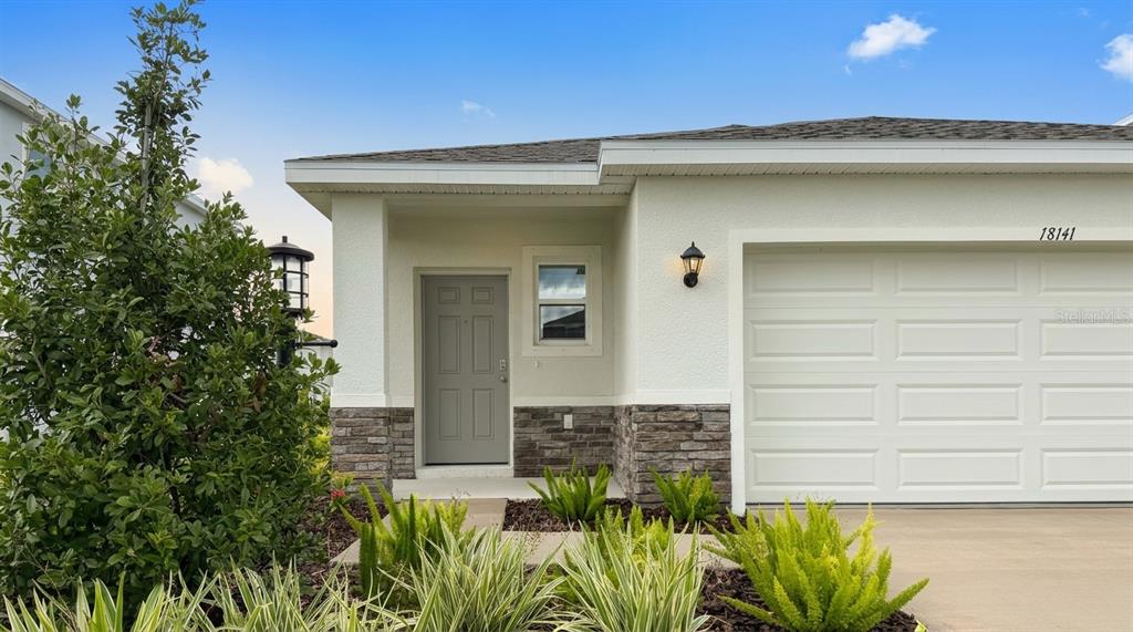 The exterior of a house features a gray front door, stone accents, and a garage — 18141 GANDER TERRACE, LAKEWOOD RANCH, FL