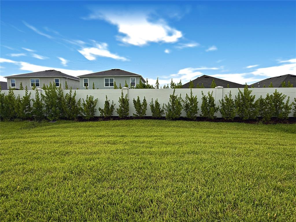 A grassy backyard features a white privacy fence lined with small green shrubs — 18141 GANDER TERRACE, LAKEWOOD RANCH, FL