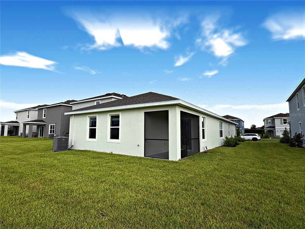 The exterior of a light-colored house features a screened-in patio and a large grassy yard — 18141 GANDER TERRACE, LAKEWOOD RANCH, FL