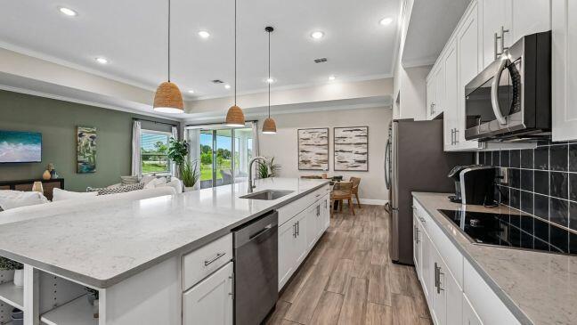 A modern kitchen features white cabinets, quartz countertops, a large island, and stainless steel appliances — 8425 101st Court, Vero Beach FL 32967, VERO BEACH, FL