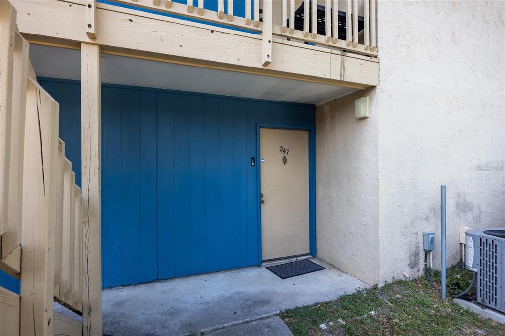 A tan door labeled 247 is set against a blue wall beneath a wooden balcony — 2811 SW ARCHER ROAD UNIT Z247, GAINESVILLE, FL