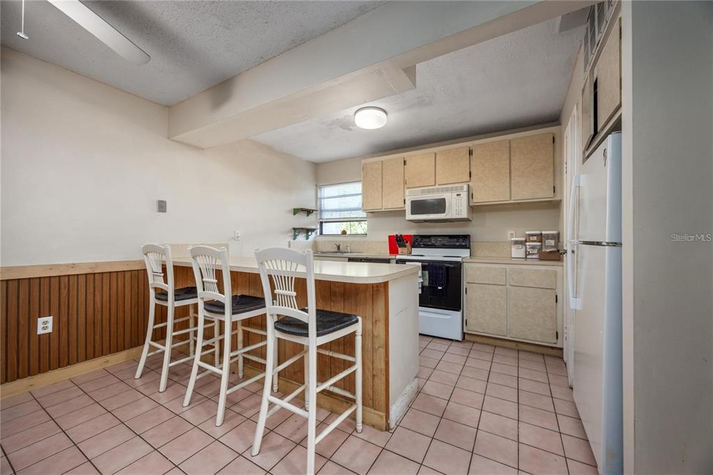 A kitchen features a breakfast bar with three chairs, light-colored cabinets, and tiled flooring — 2811 SW ARCHER ROAD UNIT Z247, GAINESVILLE, FL