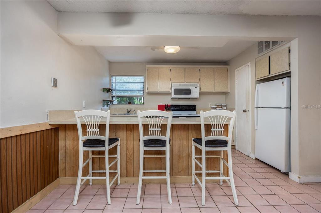 A kitchen features a breakfast bar with three chairs, wood paneling, and tile flooring — 2811 SW ARCHER ROAD UNIT Z247, GAINESVILLE, FL