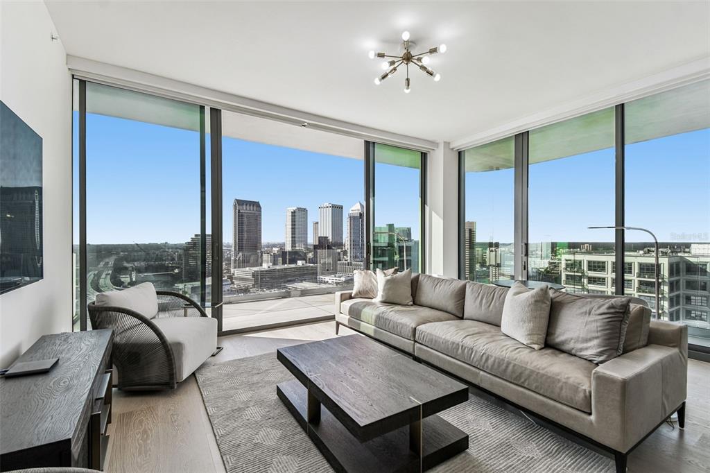 A modern living room features a large sectional sofa, coffee table, and floor-to-ceiling city views — 1000 WATER STREET UNIT 2202, TAMPA, FL
