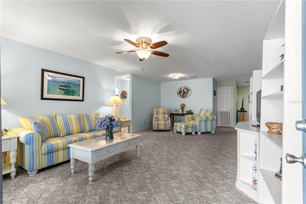 A living room features light blue walls, carpeted flooring, a striped sofa, and a ceiling fan — 8662 SW 96TH LANE UNIT A, OCALA, FL