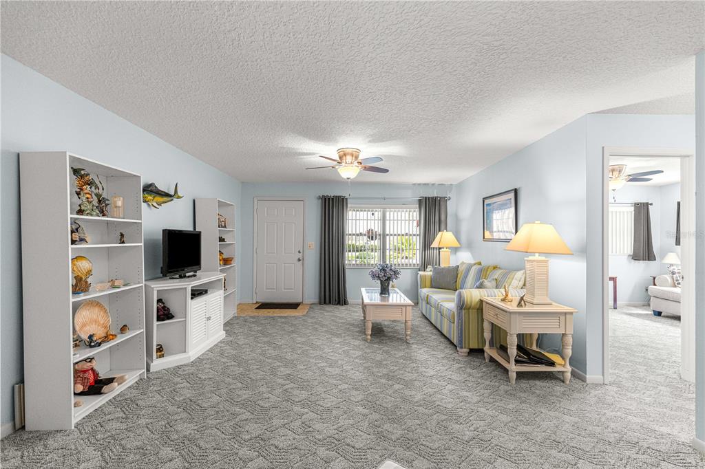 A living room features gray carpeting, a striped sofa, a white media console, and bookshelves — 8662 SW 96TH LANE UNIT A, OCALA, FL