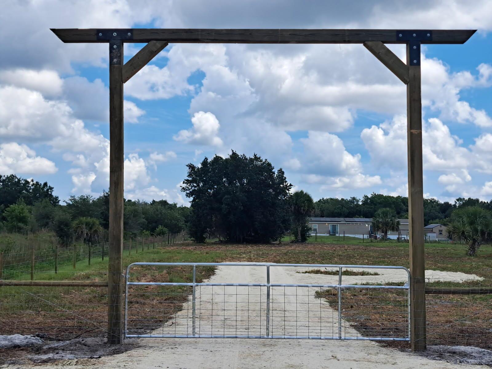 A metal gate stands beneath a wooden archway at the entrance to a rural property — 20639 NW 300th Street, Okeechobee FL 34972, OKEECHOBEE, FL