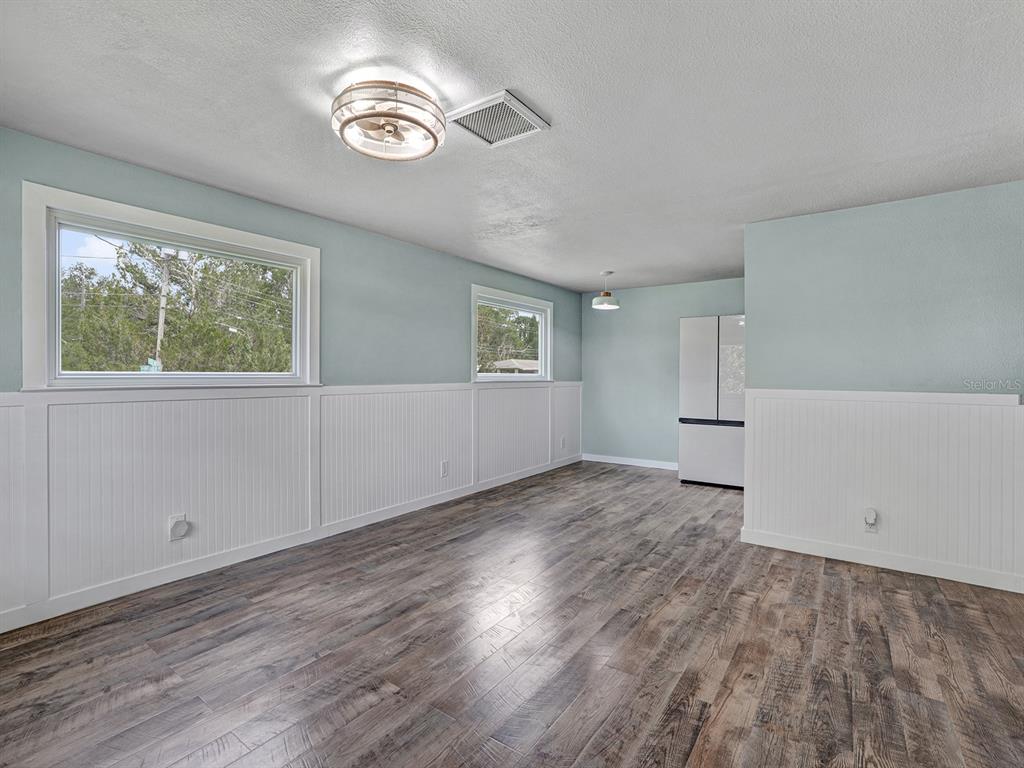 An empty room features light blue walls, white wainscoting, and wood-look flooring — 5633 ESSEX WAY, NEW PORT RICHEY, FL