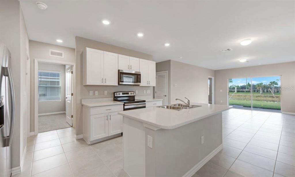 A kitchen with white cabinets, a central island, and tile flooring, opening to a living area — 18505 CRONIN SAND LANE, NORTH FORT MYERS, FL