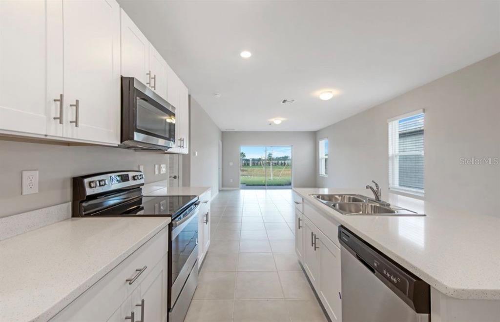 A kitchen with white cabinets, stainless steel appliances, and quartz countertops leads to a living area — 18505 CRONIN SAND LANE, NORTH FORT MYERS, FL