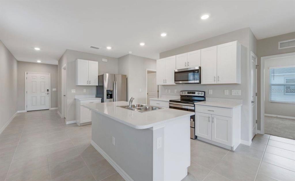 A modern kitchen features white cabinets, stainless steel appliances, a center island, and tile flooring — 18505 CRONIN SAND LANE, NORTH FORT MYERS, FL