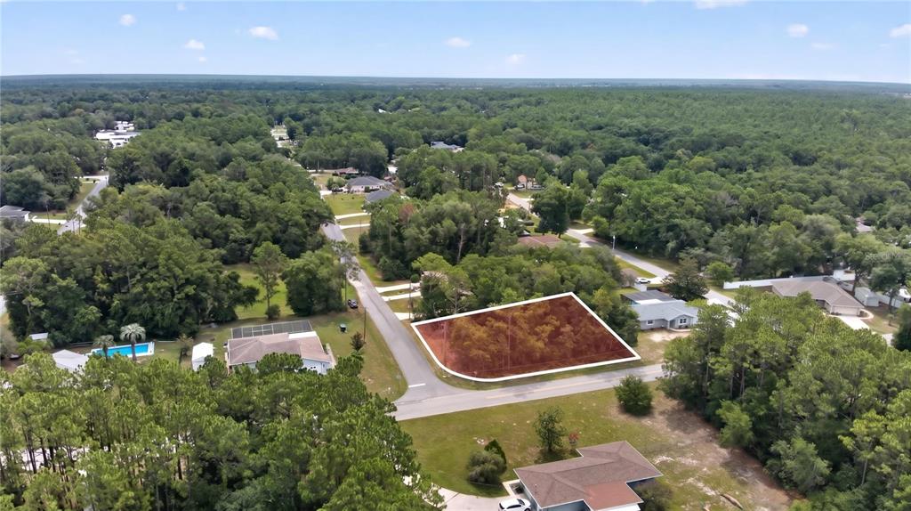 An aerial view shows a vacant, wooded corner lot highlighted in red within a neighborhood — 5056 E PRENTICE LANE, INVERNESS, FL