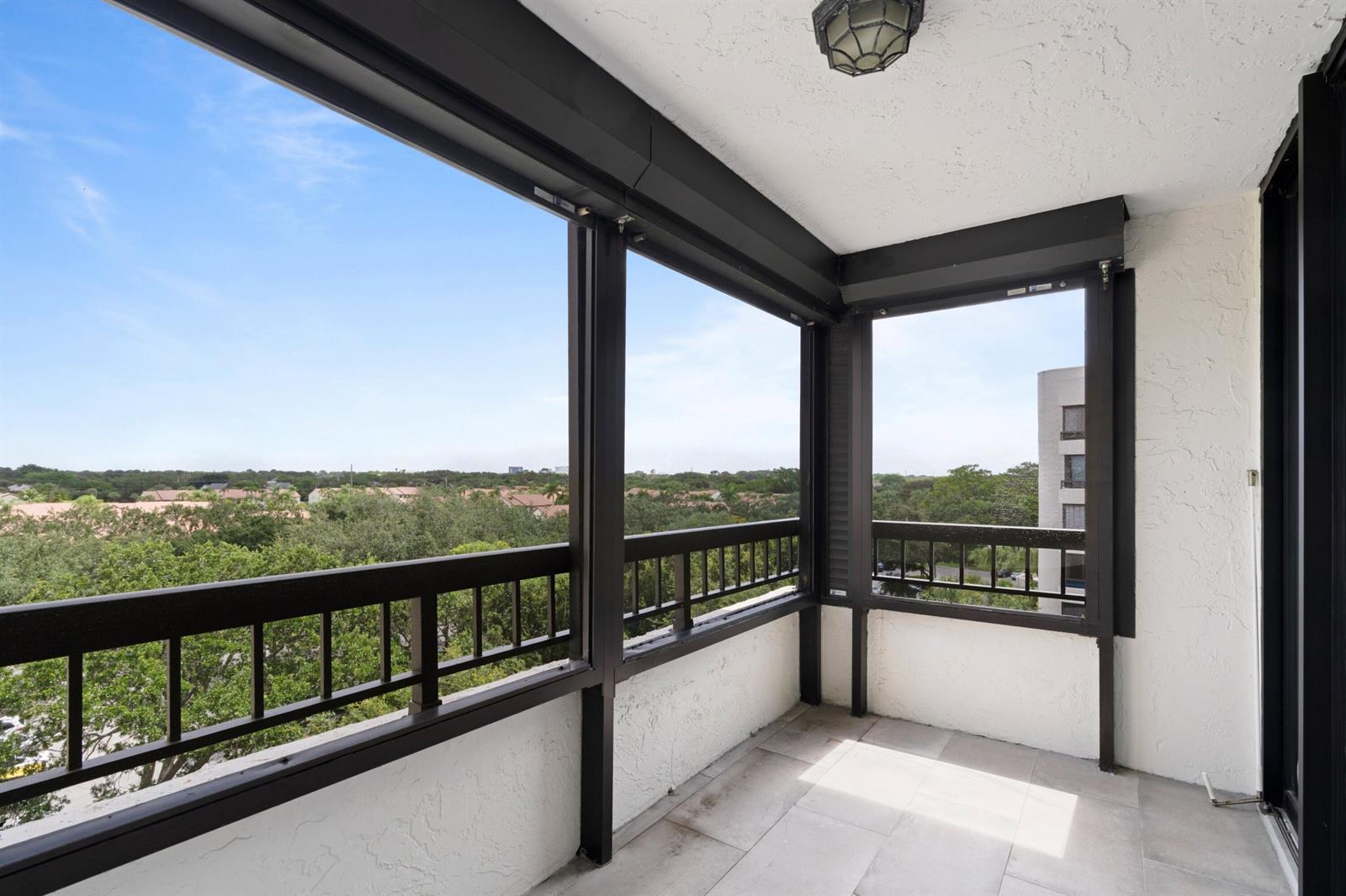 A covered balcony with dark metal railings, tiled flooring, and a view of surrounding trees — 6420 Boca Del Mar Drive # 601, Boca Raton FL 33433, BOCA RATON, FL