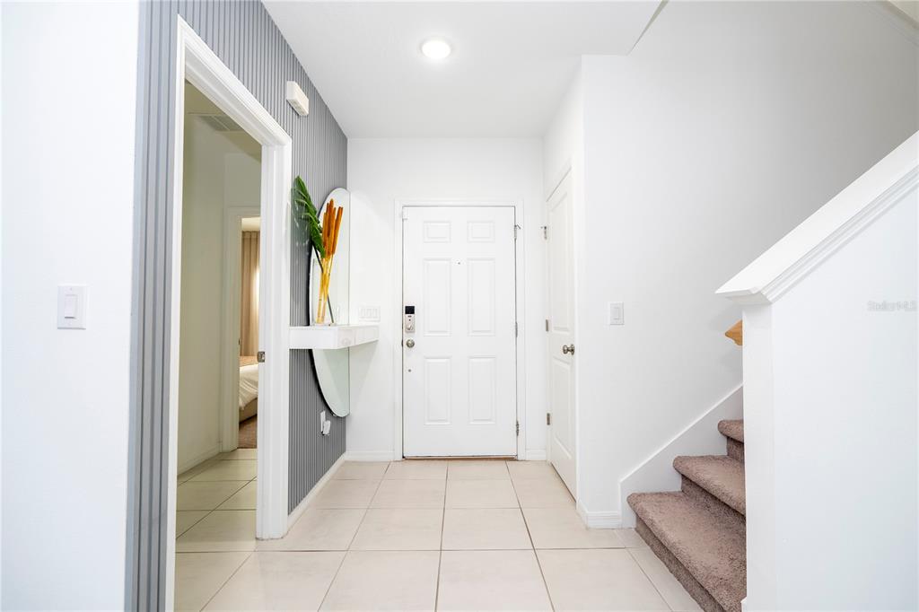 An entryway features a white front door, tiled floors, a staircase, and a decorative mirror — 5166 TUSCANY LANE, DAVENPORT, FL