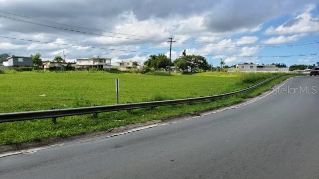 A grassy vacant lot sits next to a curved road with a metal guardrail — PR-174 SAN AGUSTIN, BAYAMON, PR