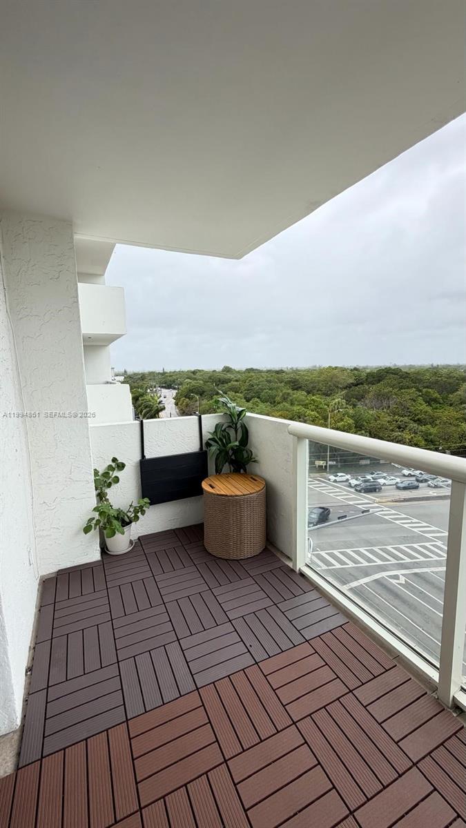 A balcony with wood-look deck tiles, a small table, a plant, and a glass railing — 13499 Biscayne Blvd # 805, North Miami FL 33181, NORTH MIAMI, FL