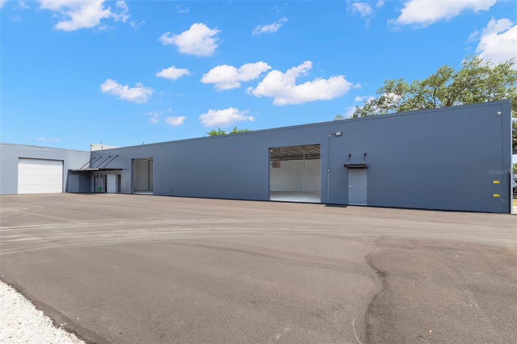 A gray industrial warehouse building features multiple roll-up doors and a large paved parking lot — 1195 KAPP DRIVE UNIT 1, CLEARWATER, FL