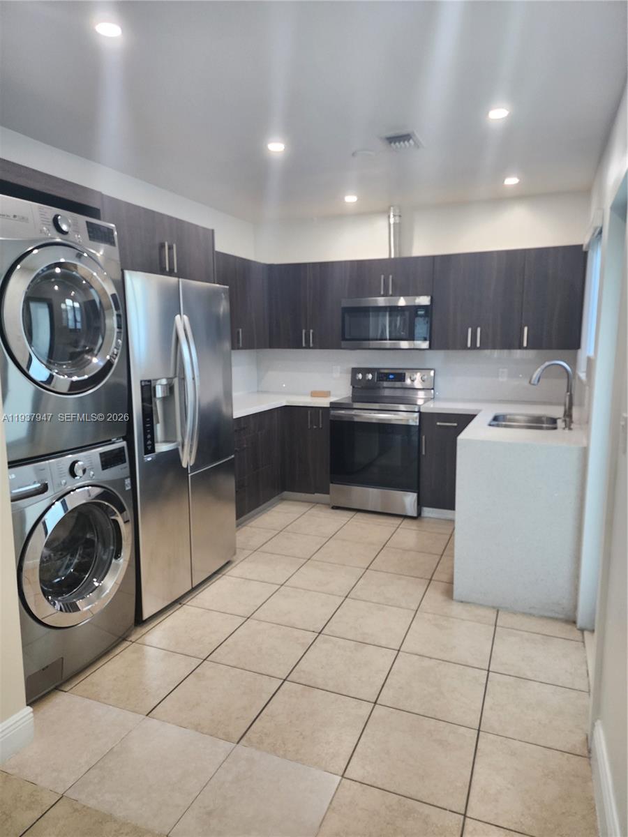 A kitchen features dark wood cabinets, stainless steel appliances, a stacked washer-dryer, and tile flooring — 310-312 SW 36th Ave, Miami FL 33135, MIAMI, FL