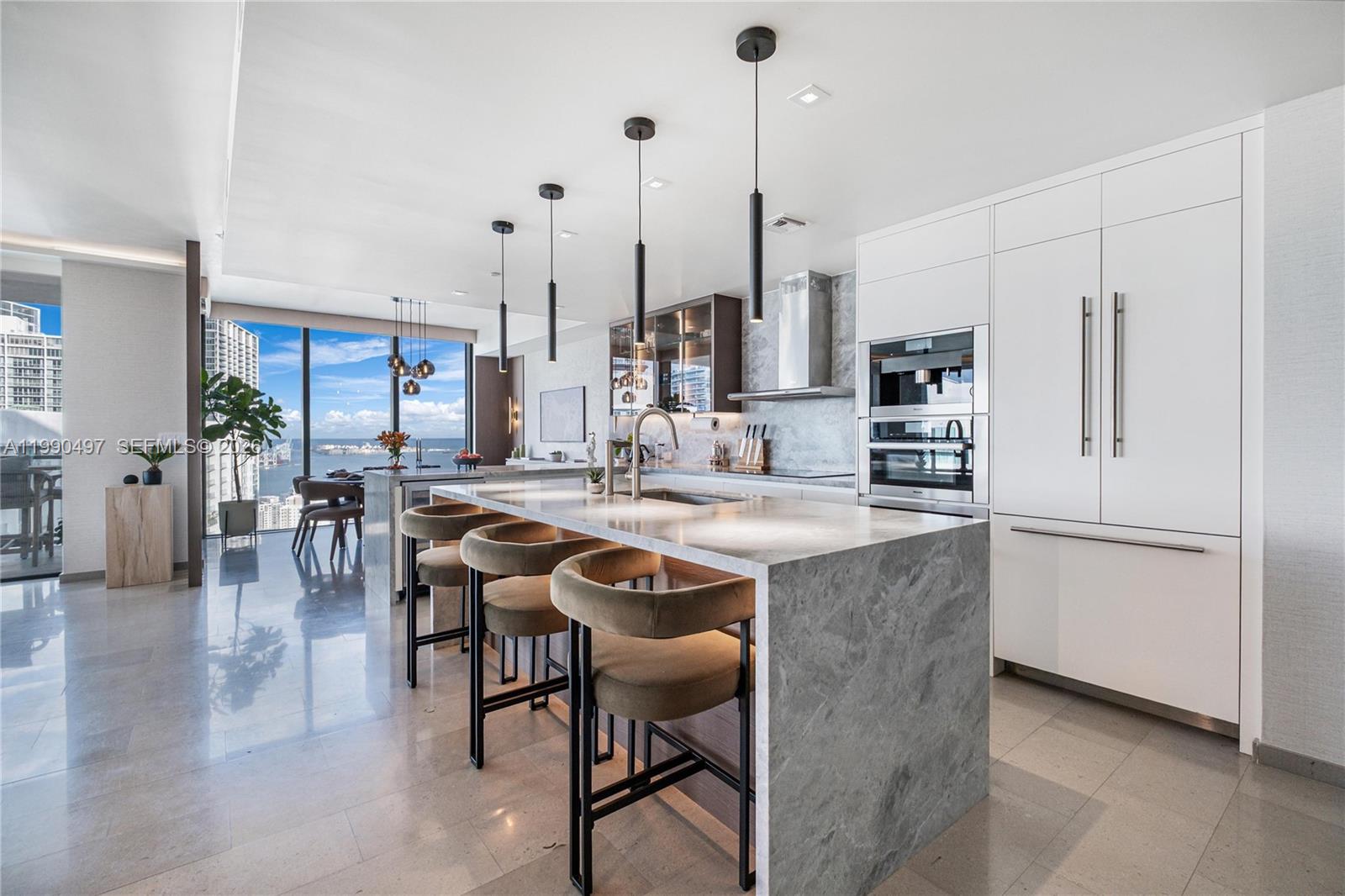 A modern kitchen features a marble waterfall island, bar stools, and floor-to-ceiling windows — 68 SE 6th St # 3711, Miami FL 33131, MIAMI, FL