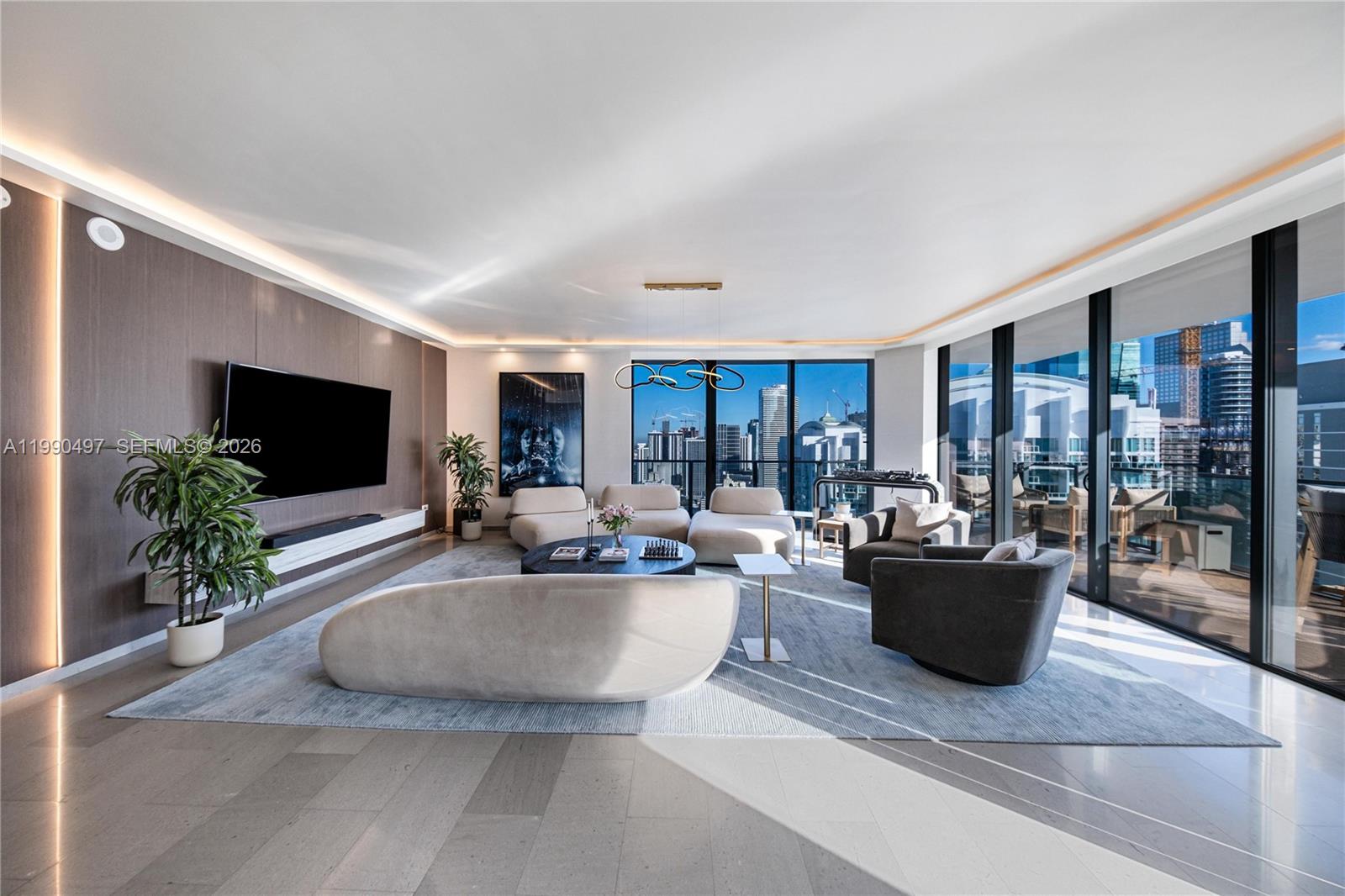 A modern living room features curved sofas, a large television, and floor-to-ceiling windows with city views — 68 SE 6th St # 3711, Miami FL 33131, MIAMI, FL