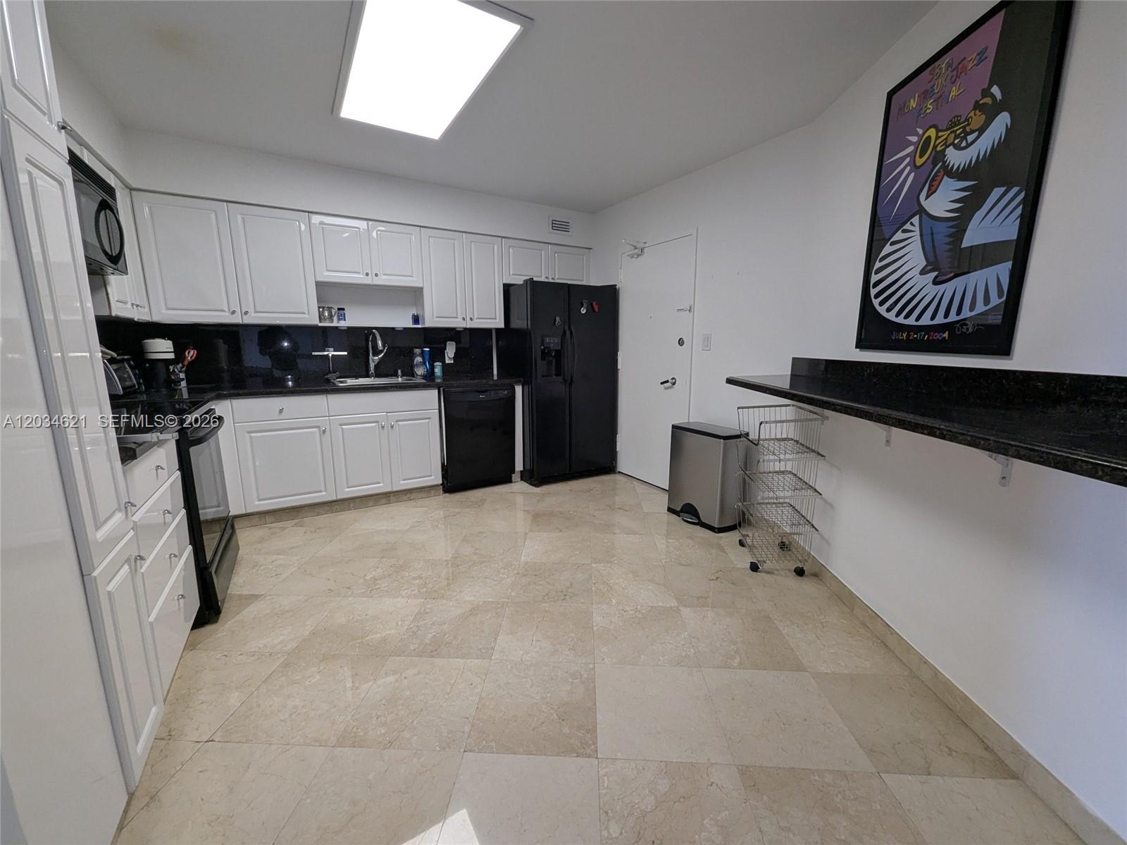 A kitchen features white cabinets, black appliances, dark countertops, and light-colored tile flooring — 5161 Collins Ave # 518, Miami Beach FL 33140, MIAMI BEACH, FL