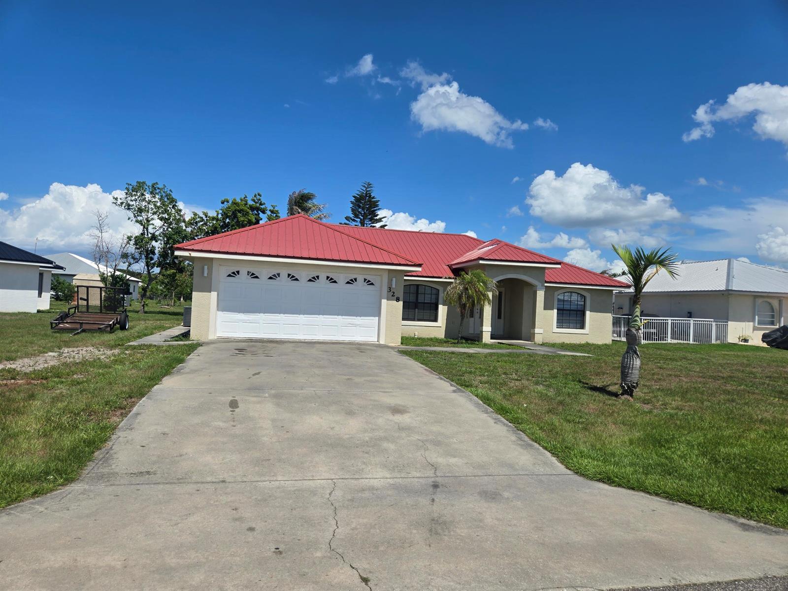 A single-story house with a red metal roof, white garage door, and concrete driveway — 328 W Sugarland Circle, Clewiston FL 33440, CLEWISTON, FL