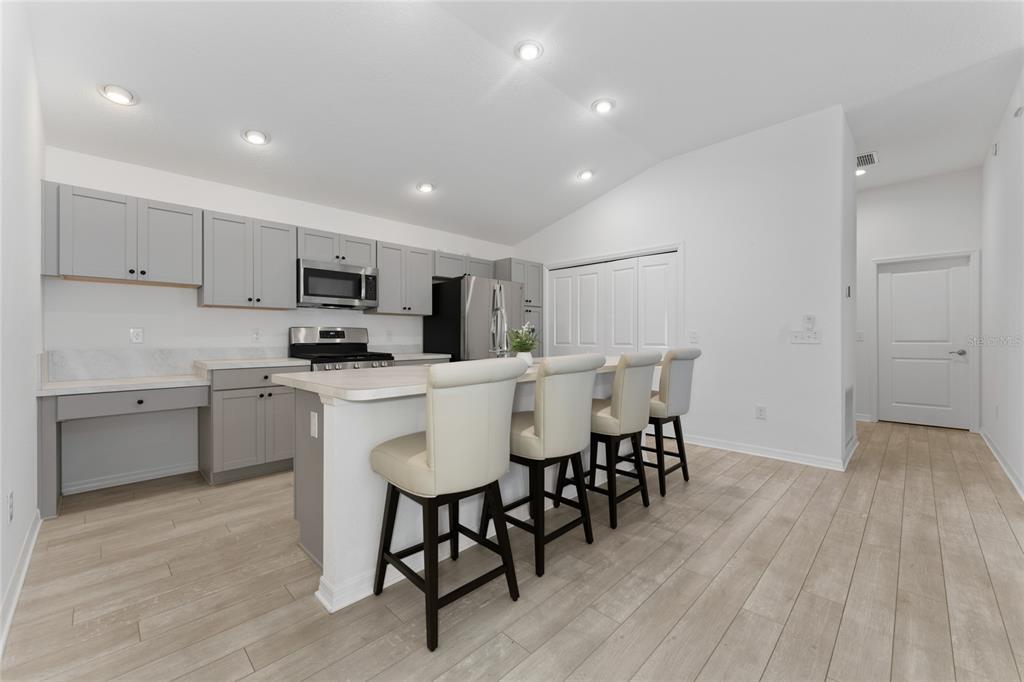A modern kitchen features gray cabinets, stainless steel appliances, a breakfast bar, and light flooring — 7634 CHERYL COURT, THE VILLAGES, FL