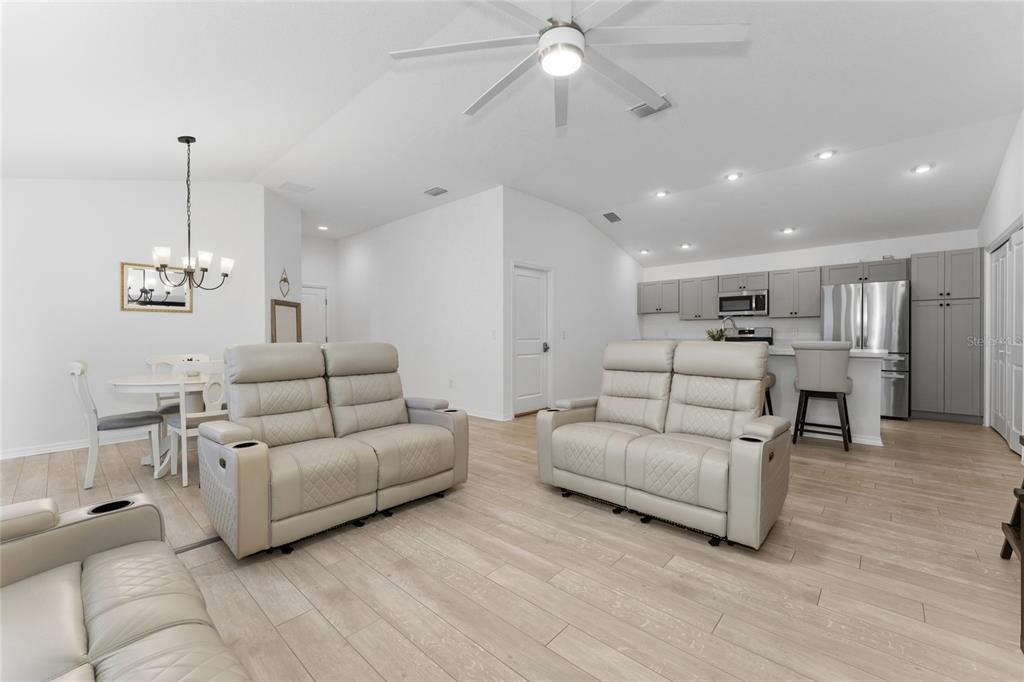 A bright open-concept living room and kitchen featuring light wood flooring and neutral furniture — 7634 CHERYL COURT, THE VILLAGES, FL