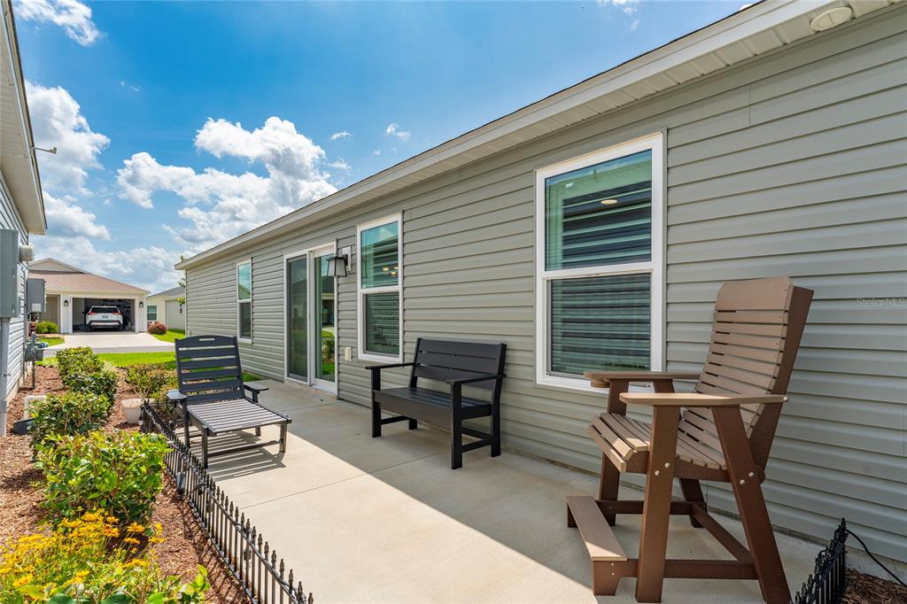 A concrete patio with outdoor furniture sits alongside the light green siding of a house — 7634 CHERYL COURT, THE VILLAGES, FL