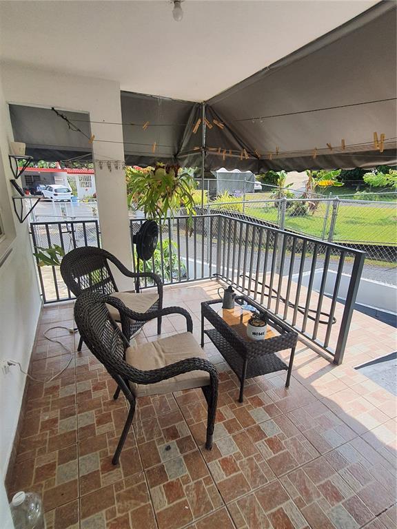 A covered outdoor balcony features tiled flooring, two wicker chairs, a small table, and railings — 2-A RIO CANAS WARD, LA BARRA COMMUNITY LOT 199, CAGUAS, PR