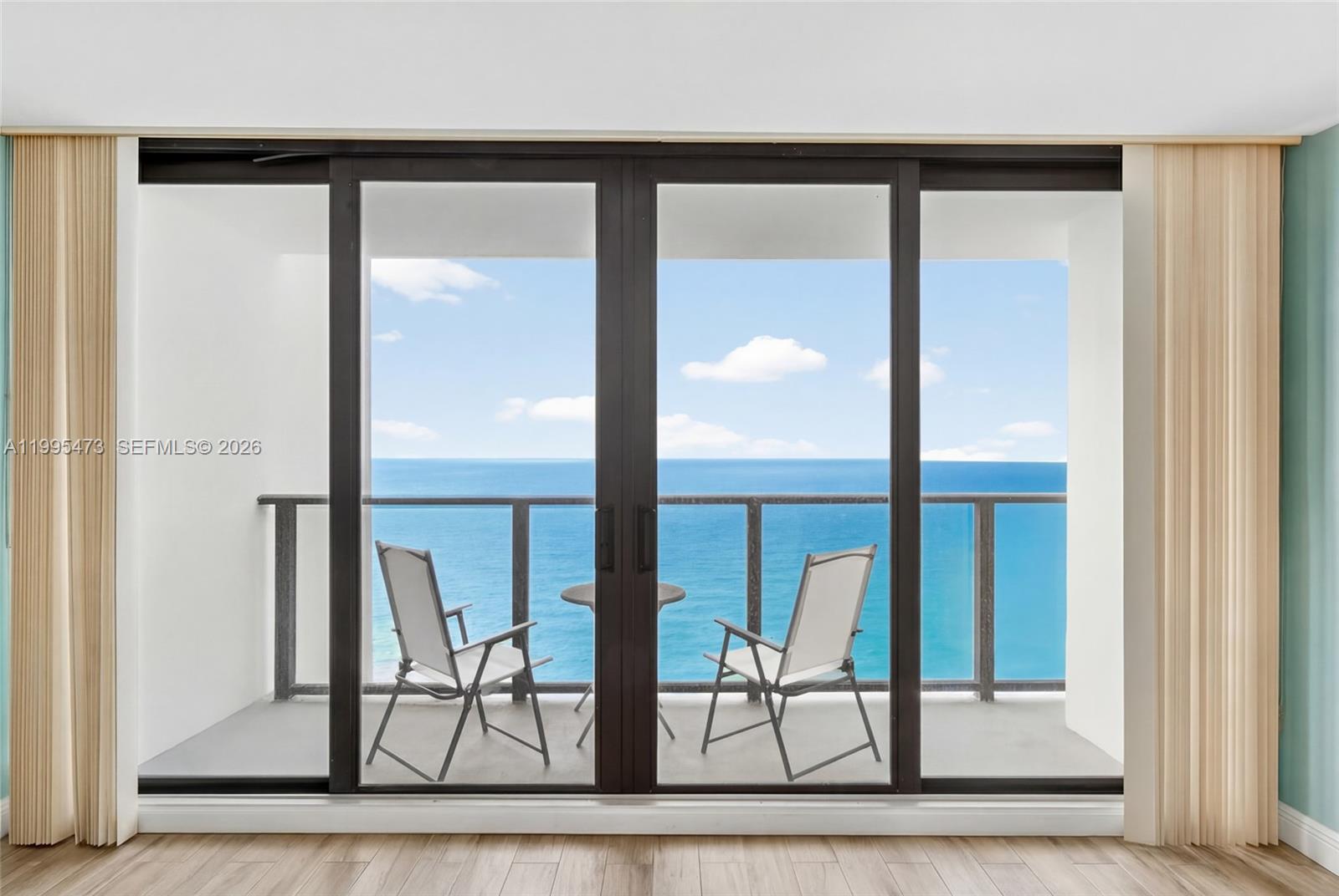 A balcony with two chairs and a small table overlooks the ocean through sliding doors — 2301 S Ocean Dr # 2302, Hollywood FL 33019, HOLLYWOOD, FL