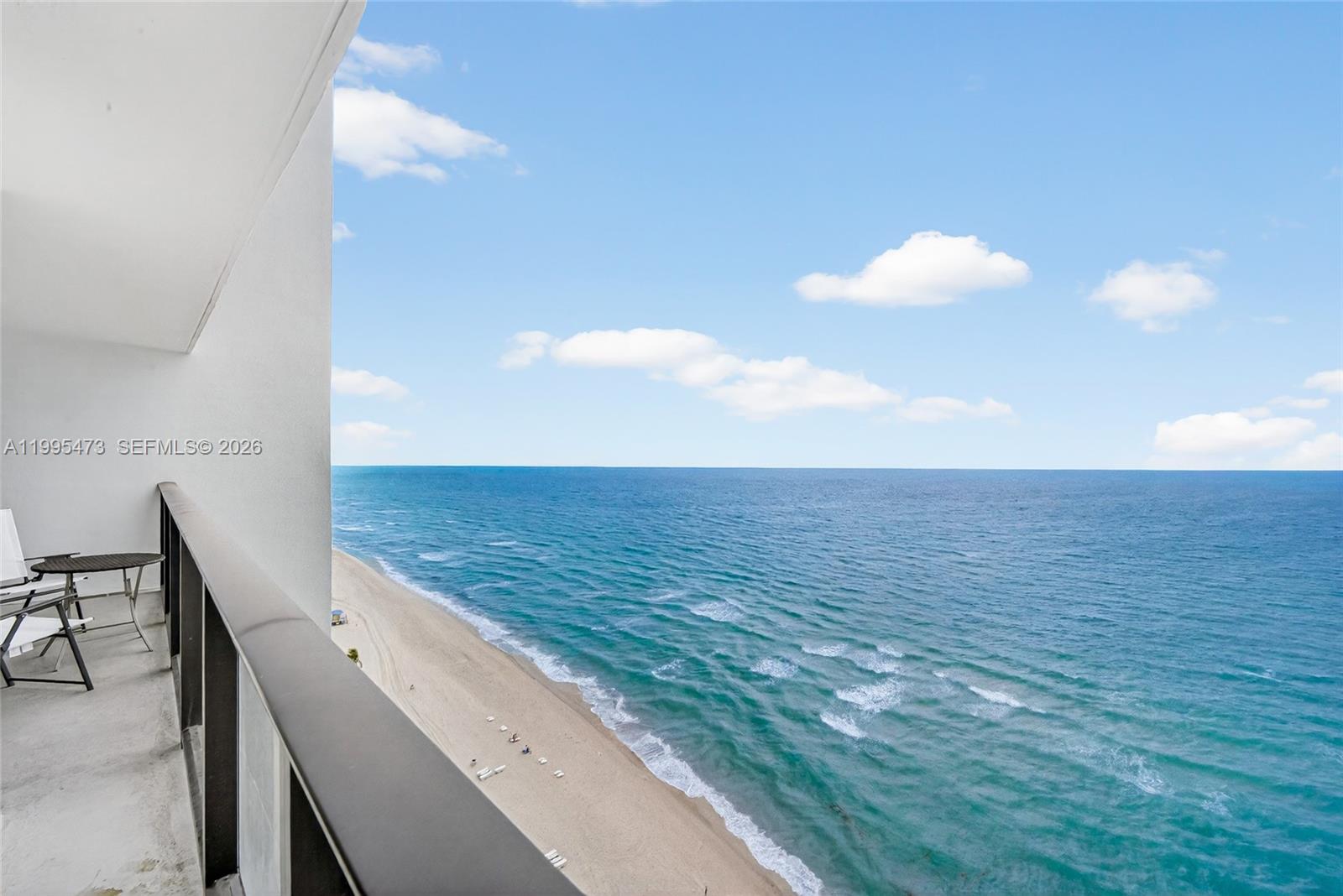 A high-rise balcony overlooks a sandy beach and the blue ocean under a clear sky — 2301 S Ocean Dr # 2302, Hollywood FL 33019, HOLLYWOOD, FL