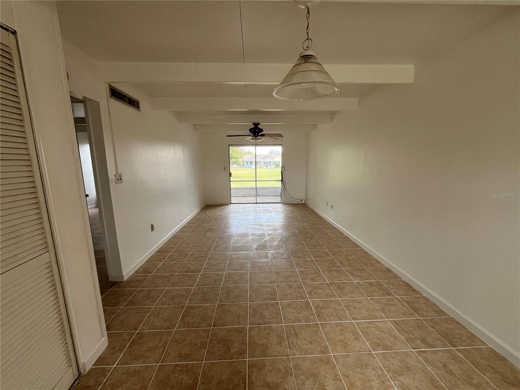An empty room with white walls, tiled floors, exposed ceiling beams, and a sliding glass door — 1707 CLUB CIRCLE UNIT 1707, LAKESHORE, FL