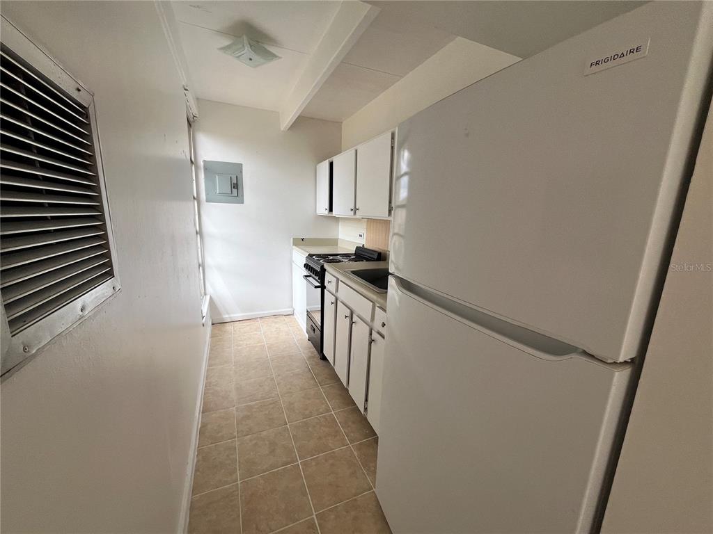 A narrow galley kitchen features white cabinets, a Frigidaire refrigerator, and tiled flooring — 1707 CLUB CIRCLE UNIT 1707, LAKESHORE, FL