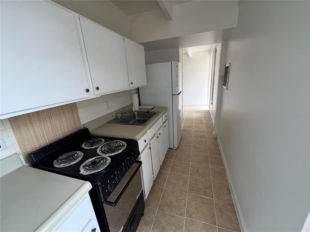 A galley kitchen features white cabinets, a black stove, a stainless sink, and tiled flooring — 1707 CLUB CIRCLE UNIT 1707, LAKESHORE, FL