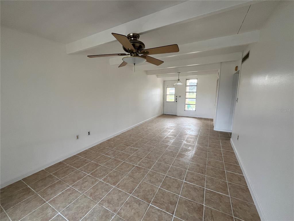 An empty room with white walls, tiled flooring, exposed ceiling beams, and a ceiling fan — 1707 CLUB CIRCLE UNIT 1707, LAKESHORE, FL