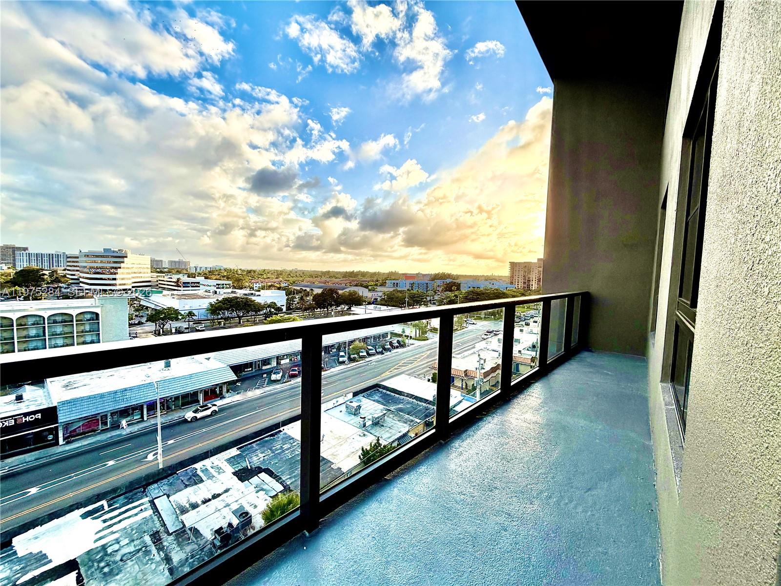 A high-angle view from a balcony overlooking a city street and buildings under a cloudy sky — 1650 NE 124th St # 621, North Miami FL 33181, NORTH MIAMI, FL