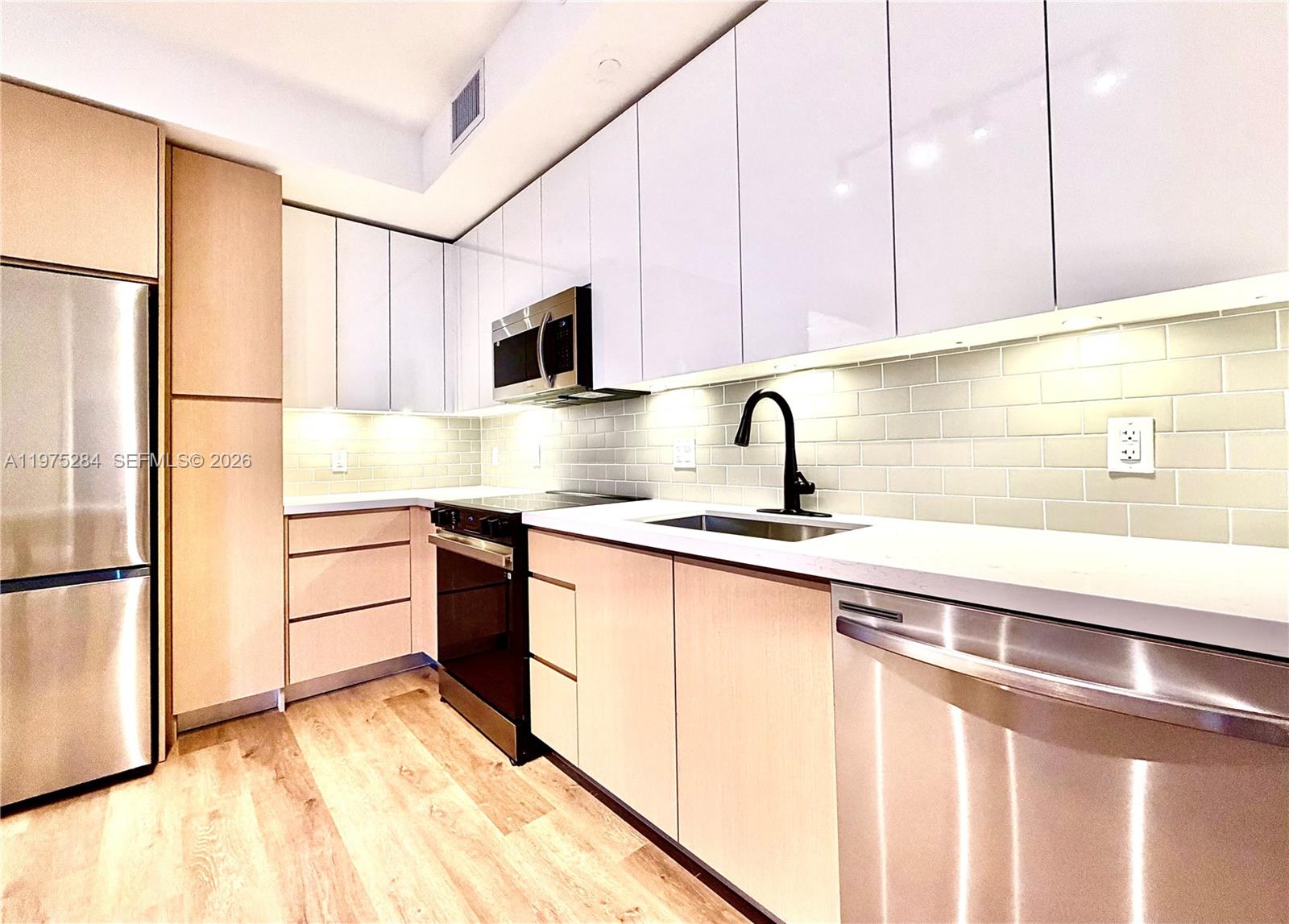 A modern kitchen features light wood cabinetry, white upper cabinets, stainless steel appliances, and backsplash — 1650 NE 124th St # 621, North Miami FL 33181, NORTH MIAMI, FL