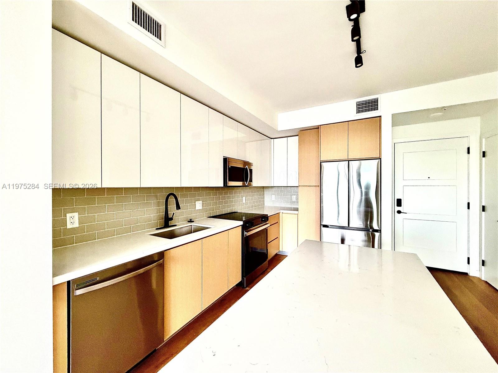 A modern kitchen features white upper cabinets, light wood lower cabinets, and a large island — 1650 NE 124th St # 621, North Miami FL 33181, NORTH MIAMI, FL