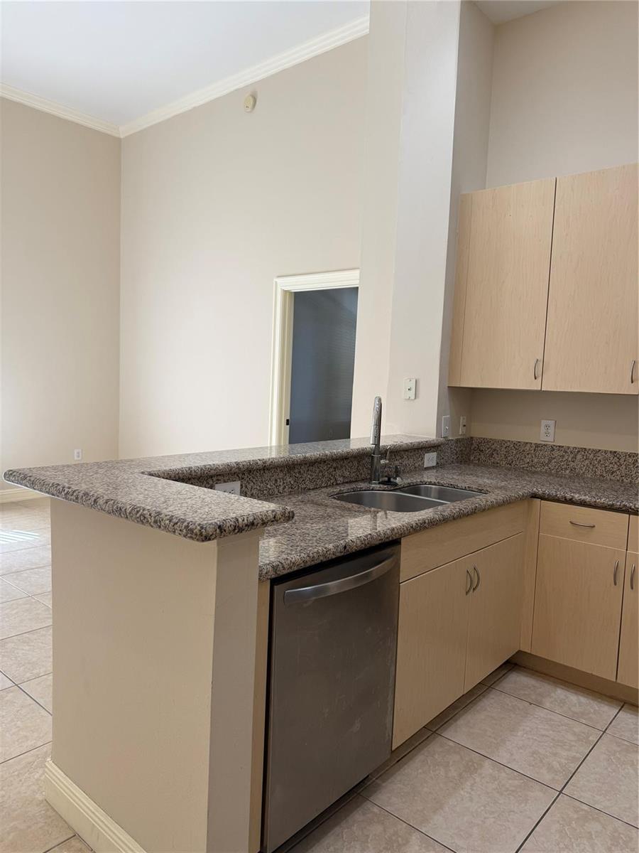A kitchen features light wood cabinets, granite countertops, a stainless steel dishwasher, and tile flooring — 16102 Emerald Estates Drive # 103, Weston FL 33331, WESTON, FL