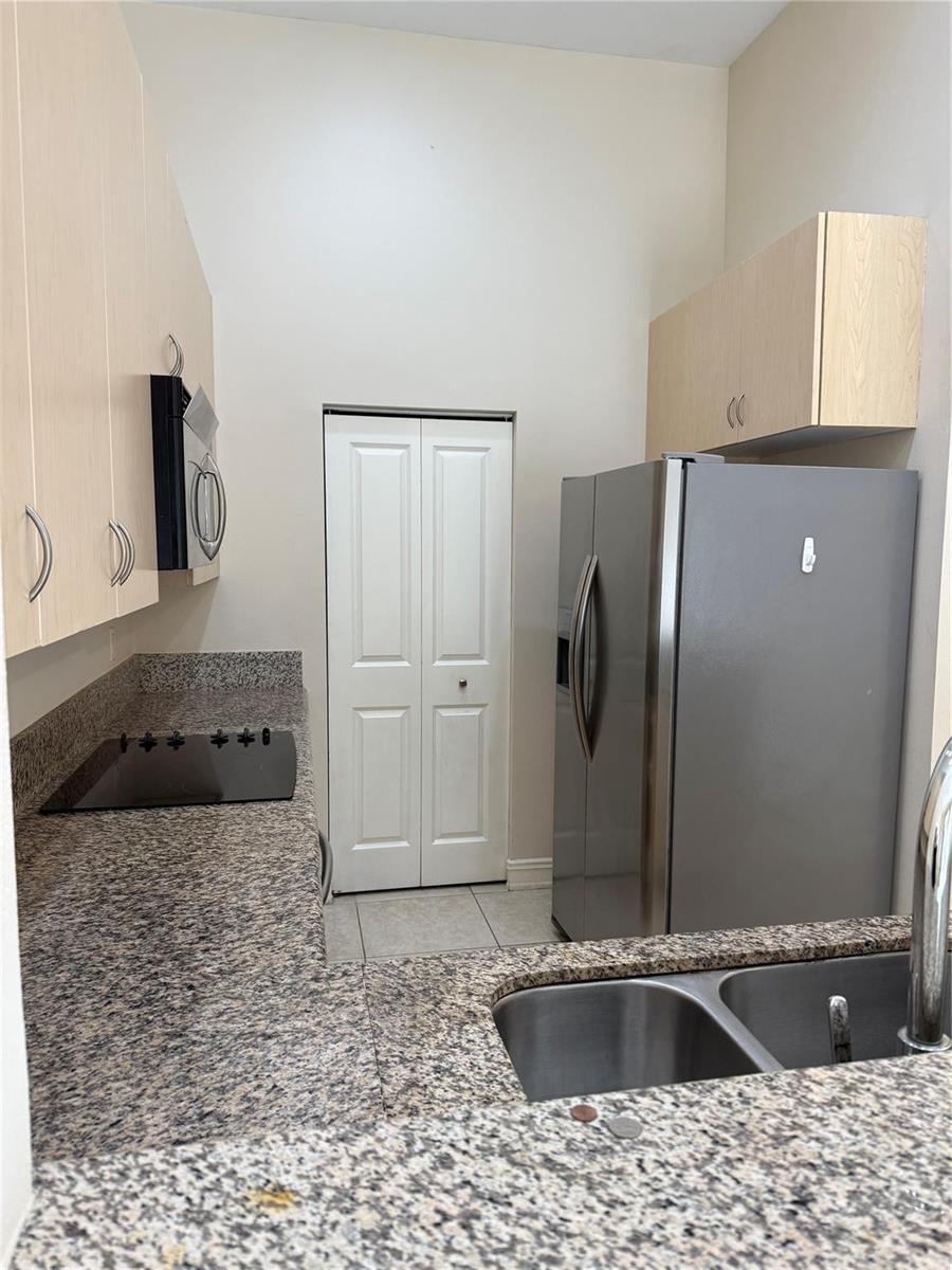 A kitchen features light wood cabinets, granite countertops, stainless steel appliances, and a pantry door — 16102 Emerald Estates Drive # 103, Weston FL 33331, WESTON, FL