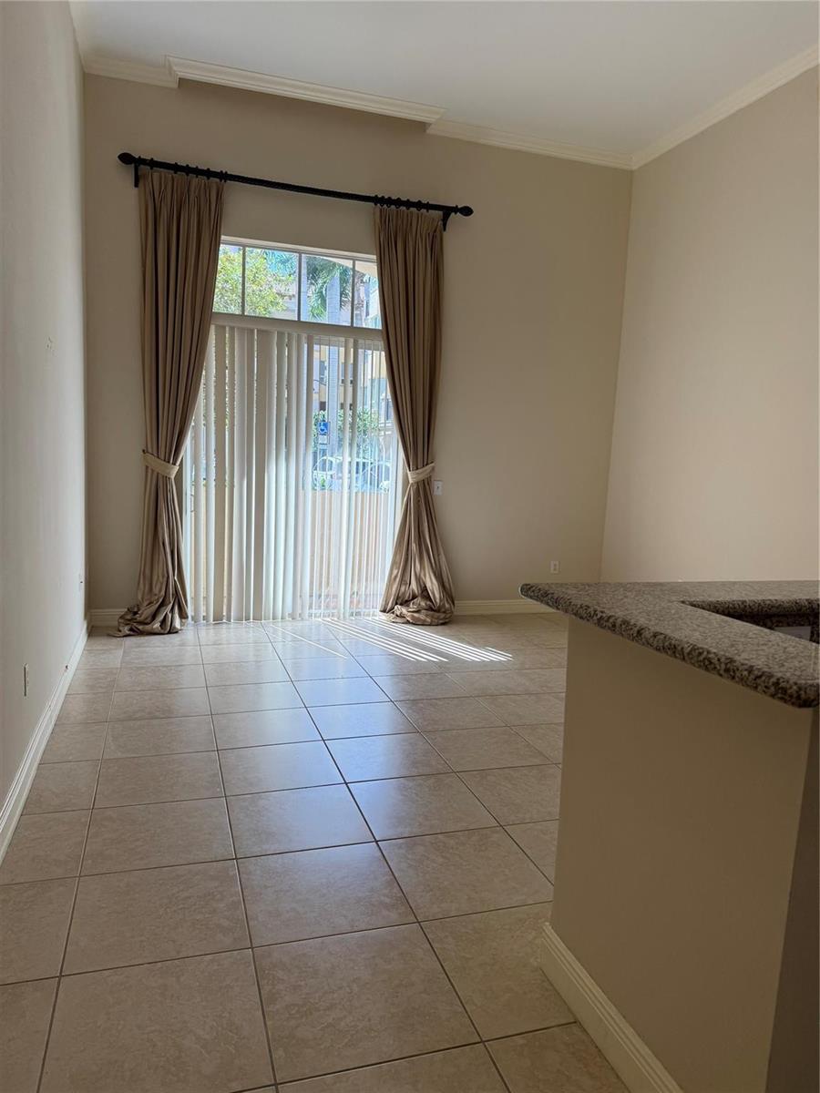 An empty room with tile flooring, a granite-topped counter, and sliding glass doors with curtains — 16102 Emerald Estates Drive # 103, Weston FL 33331, WESTON, FL